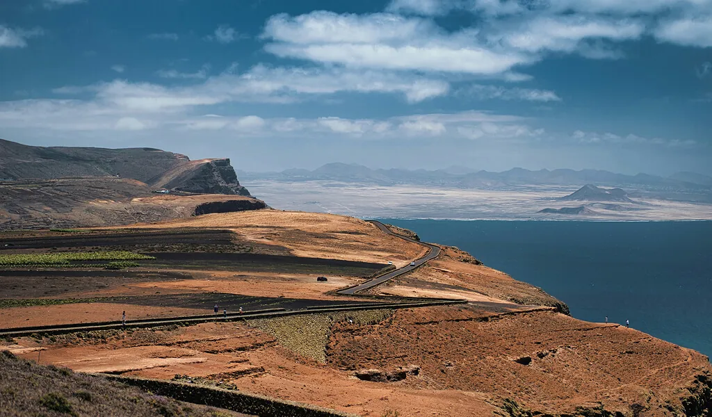 Straße durch die karge Vulkanlandschaft Lanzarotes mit Blick auf den Atlantik