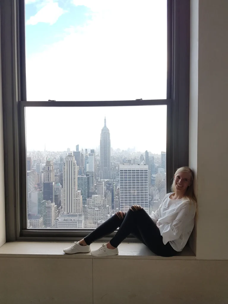 Reiseberaterin sitzt am Fenster mit Blick auf das Empire State Building und die Skyline von Manhattan