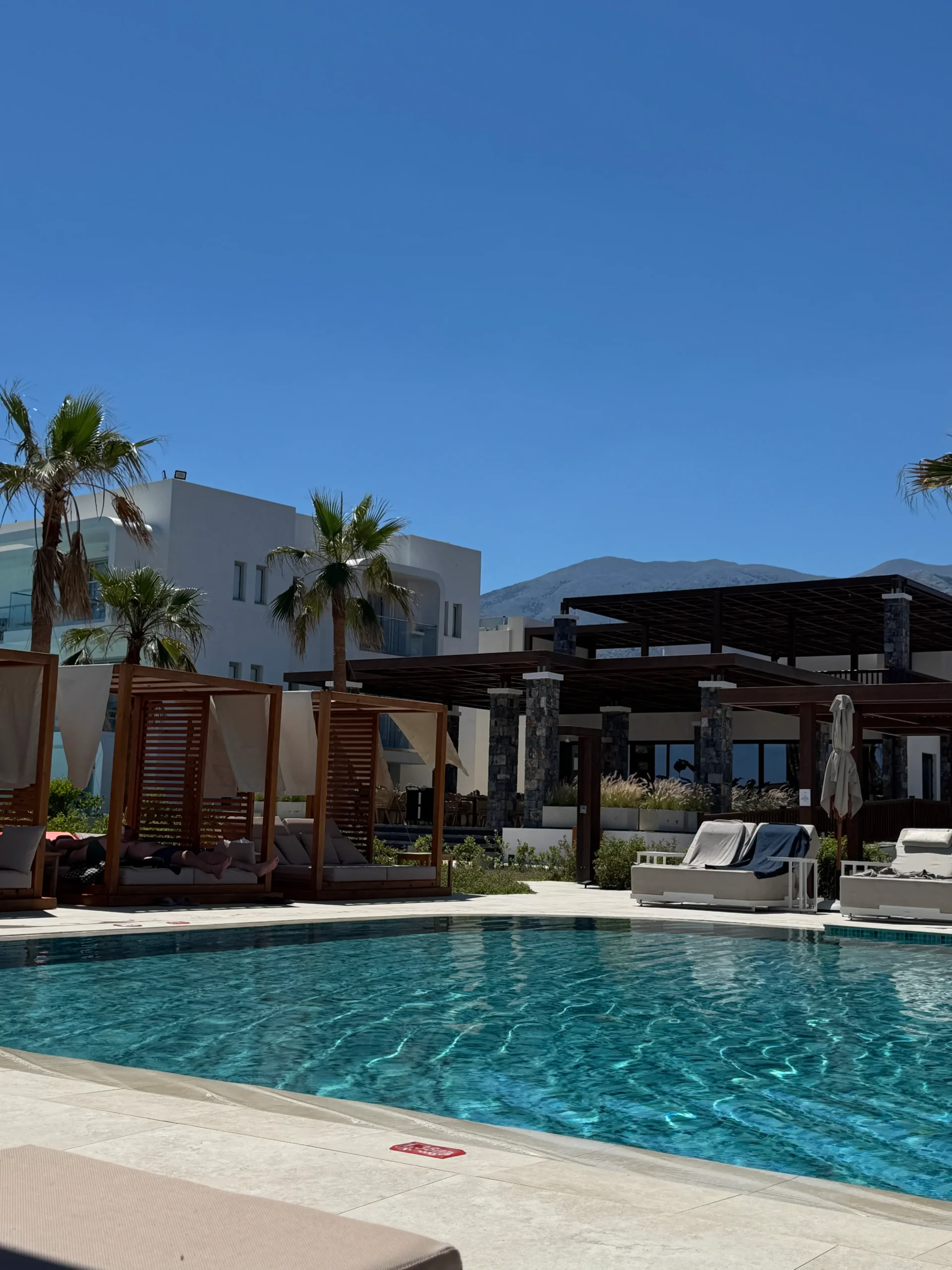 Pool des allsun Hotel Carolina Sun Beach mit Sonnenliegen, Palmen und kretischer Bergkulisse