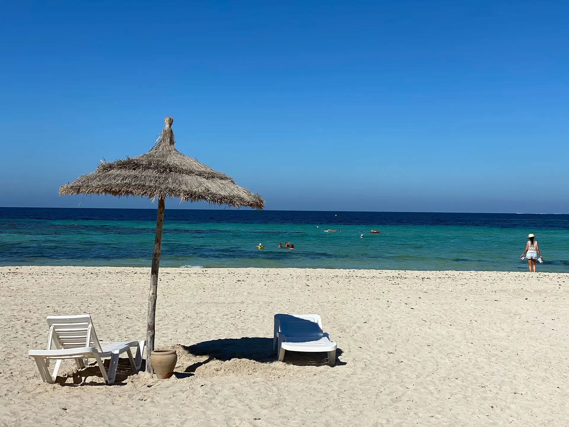 Sandstrand auf Djerba in Tunesien mit Sonnenschirm, Liegen und türkisblauem Meer.